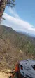 The image captures a scenic mountainous landscape viewed from behind the seat of an off-road vehicle, with a clear blue sky above and trees beginning to show spring growth.