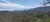 A scenic landscape showcasing lush greenery, rolling hills, and a mountain range under a partly cloudy sky.
