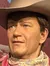 A person is standing next to a life-sized cowboy figure in a desert-themed display.