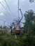 People are riding on a chairlift over a green landscape under a cloudy sky.