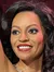A wax figure of a woman with an outstretched pose and a smiling expression is in the foreground, while a wax figure of a man seated at a piano is in the background, all set against a brick wall backdrop with a disco ball overhead.
