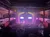 The image shows the interior of a theater with a brightly lit stage, audience seating, and private boxes, possibly during an event or performance.