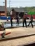 Individuals dressed as lumberjacks are competing in a log rolling event in an outdoor venue with a water pool and lumberjack-themed decorations.