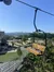 A chairlift with an empty seat overlooks a vibrant outdoor recreational area with people walking, set against a backdrop of lush mountains under a clear blue sky.