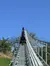 A roller coaster car ascends a steep track towards the summit against a clear blue sky.