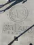 This image shows a concrete surface with an embossed logo reading 'SLR' inside a circle and 'SKYLAND RANCH' below it, with the shadow of a pole diagonally across the photo, and the feet of two people at the top edge.