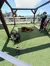 A person is standing in a shaded outdoor area with artificial turf where a dog is lying down near a fan, possibly cooling off on a sunny day.