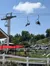 People are enjoying a chairlift ride above a scenic park area on a sunny day.