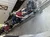 The image depicts a row of people sitting in a virtual reality roller coaster simulation, wearing VR headsets and secured by over-the-shoulder restraints.