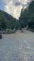 A group of people on all-terrain vehicles are on a gravel road near a forested hillside.