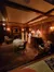 The image shows a dimly lit vintage-style room setting with mannequins dressed in period clothing, antique furniture, and elegant table settings, suggestive of an exhibit or historical display.