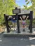 Two individuals are playfully posing with their heads and hands in wooden stocks under a sign that labels them as