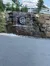 The image shows an artificial waterfall cascading over a rock wall with the initials 