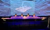 A model of the RMS Titanic is displayed before a backdrop of underwater imagery, likely as part of an exhibition.