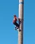 The image shows a person climbing a tall, smooth pole against a clear blue sky.