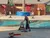 A person is demonstrating log rolling in a pool with a logging-themed backdrop and equipment, including chainsaws and target boards, as part of an entertainment show.