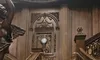The image shows an elegant wooden staircase with intricately detailed iron railings, leading to a wall with a clock and ornate wooden carvings, inside a luxurious interior setting.