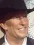 A person is smiling next to a life-sized figure of a cowboy-hat-wearing guitarist against a colorful mural background.
