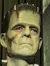 A person is embracing a life-size Frankenstein's monster figure in a staged environment with dramatic lighting.