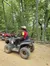 A person is sitting on an all-terrain vehicle (ATV) on a dirt path in a forested area.