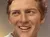 A person is taking a selfie with a lifelike wax figure that resembles a cheerful young man.