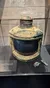 The image shows an old, corroded starboard navigation light with a wick and wick holder, likely recovered from a sunken vessel, displayed in a museum setting.