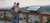 An adult and a child are overlooking a scenic valley from a wooden observation deck with an informational plaque in view.