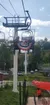 Two people are sitting on a chairlift with a decorative American flag banner, ascending over a grassy area with a walking path below.