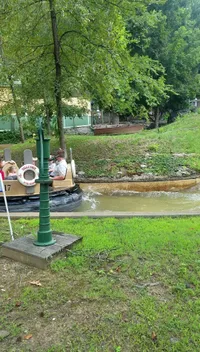The image shows a small group of individuals enjoying a ride in a theme park water attraction, surrounded by lush greenery.