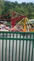 The image captures a colorful amusement park ride in motion with people enjoying it, fenced off from the viewer by a green barrier.