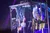 People are performing an upside-down act on a stage structure, with dramatic lighting enhancing the scene.