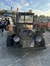 An old, rustic car decorated with various items and signs is parked in a lot while people walk by.