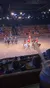 People in colorful medieval-style costumes are riding horses in an indoor arena, performing for an audience who are seated around banquet-style tables.