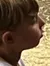 A young boy sits attentively on a stump, looking up at a man who is crouched down to speak with him, with wood chips scattered on the deck and a placid pool of water in the background reflecting part of the scene.