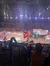 The image shows a dynamic scene at a themed show with performers dressed in colorful costumes riding horses and carrying flags, with an audience watching from tiered seating around an arena.