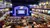 The image shows a crowded theater with an audience seated at tables and a decorated stage set for a performance, with