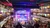 Audience members enjoy a lively performance in a spacious theater with multiple seating levels and a festively-lit stage.