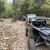 A line of off-road vehicles travels along a rocky forest trail.
