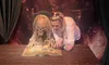 A person is leaning over a large open book alongside a scary, realistic-looking figure at what appears to be a themed attraction or exhibit.