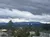 The image shows a landscape view of overcast skies above a mountain range with urban elements like street lamps and fencing in the foreground.