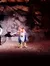 The image shows a person in a theatrical costume performing on a stage with a rocky-like backdrop, possibly as part of a play or live show.