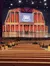 The image showcases the interior of the Grand Ole Opry, featuring its iconic stage and empty audience seating area.