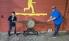 A boy and a man are posing with a large two-handled saw in front of a wooden wall with a yellow lumberjack silhouette at the Lumberjack Feud attraction.