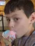 A young person is sitting at a wooden table inside a spacious, rustic building, enjoying a cone of sprinkle-covered ice cream.