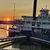 A paddle-steamer riverboat is docked at a pier during sunset, with people on the decks enjoying the view.