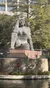 This image shows a large, modern-style statue of a seated figure with a star on its forehead near a body of water, with greenery and a building in the background.