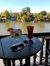 Two cocktails are placed on a small round table on a balcony overlooking a serene river, with sunglasses suggesting a bright sunny day.