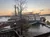 A paddlewheel riverboat is docked at a pier during sunset, with barren trees and a serene water backdrop.