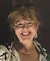 A person is smiling while standing inside the open jaws of a large shark model.