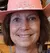 Two smiling individuals are posing with pink cowboy hats and holding stuffed animal souvenirs in a store filled with various styles of cowboy hats.